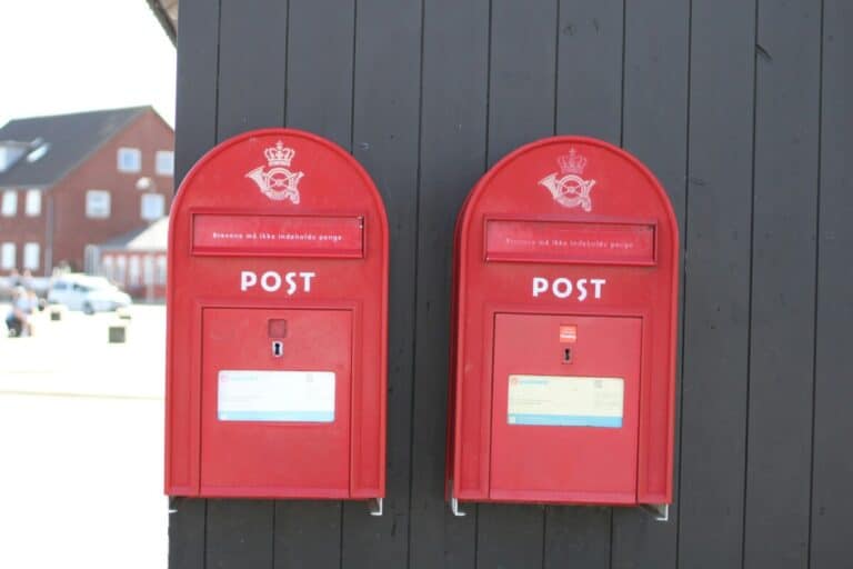 Two red Danish postboxes side by side on a wooden building in the snow.